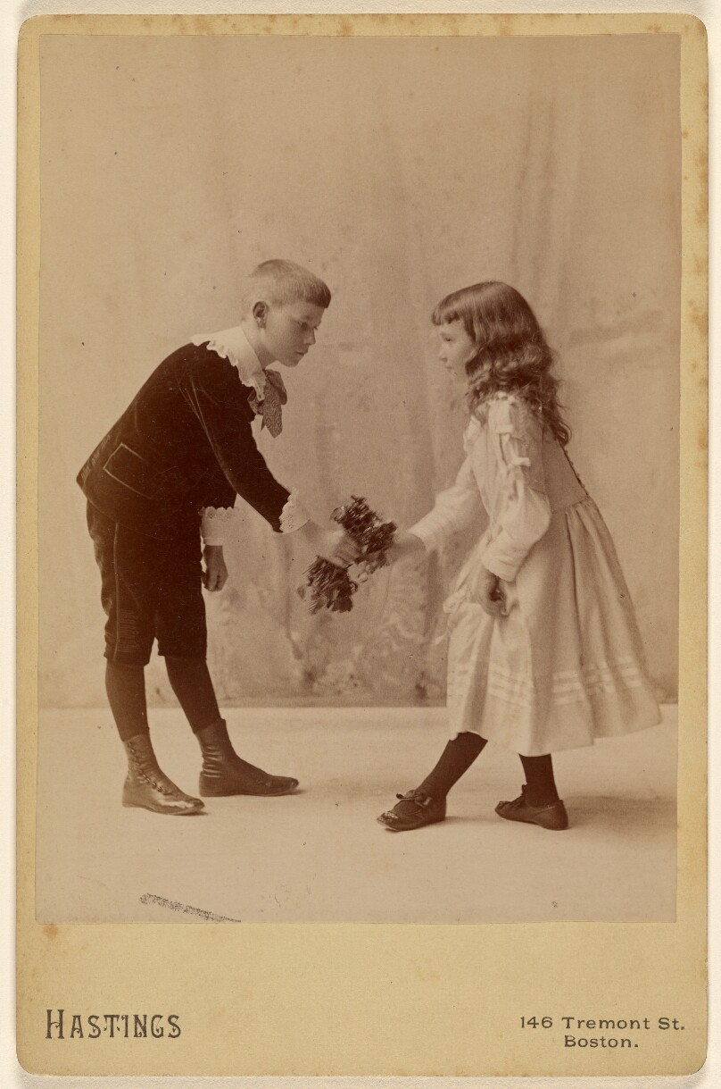 [Young boy presenting bouquet to young girl, both bowing]