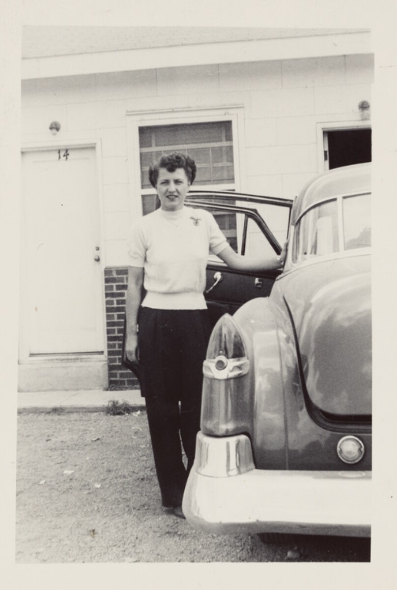 [Woman posed beside car]