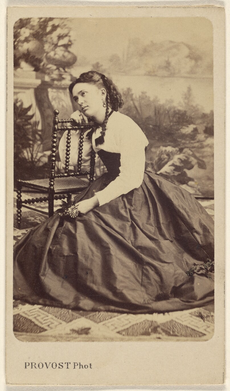 [Unidentified young woman kneeling on floor, head to chair back]