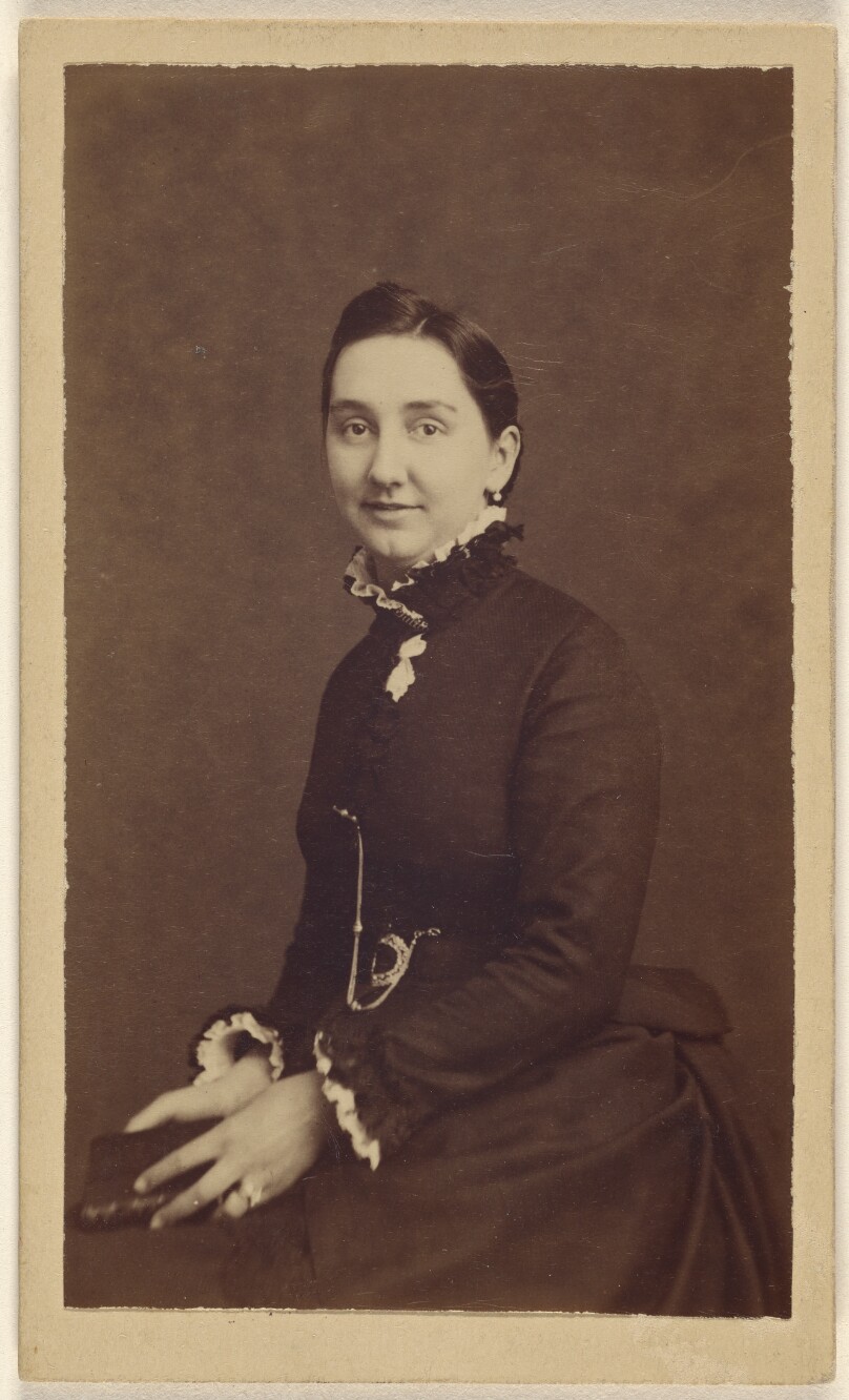 [Unidentified woman wearing a dark dress, holding a book, seated]