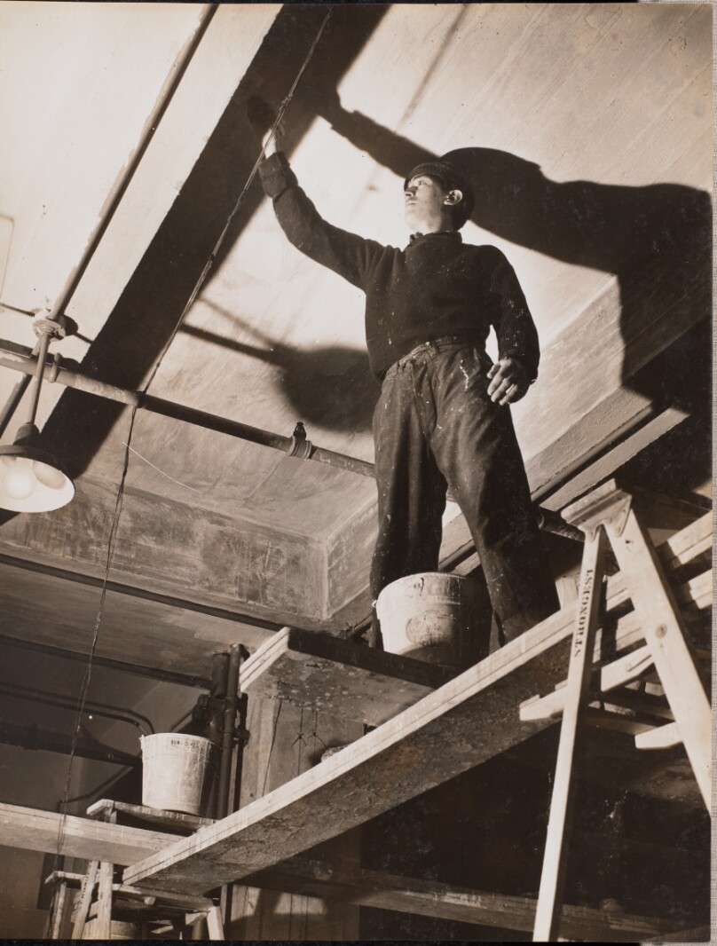 [Man standing on wooden scaffolding paints a ceiling]