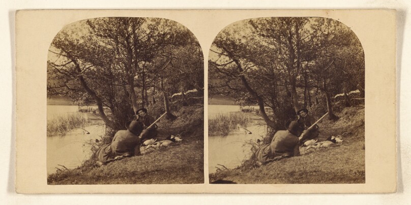 [Two men sitting on a river bank, one man holding a shotgun]