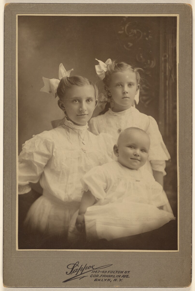[Three children: two girls standing, baby in foreground]