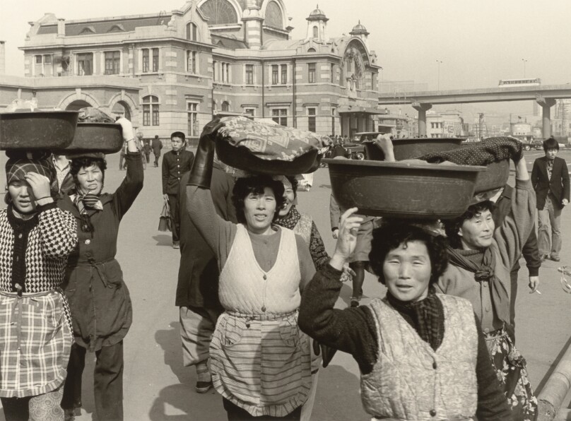 [Group of Women in Aprons Carrying Trays of Clothes on Their Heads, Walking Away from Seoul Station]