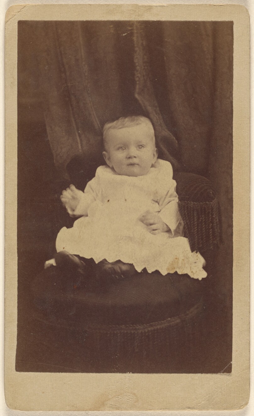 [Unidentified baby seated in dark-colored chair with tassels]