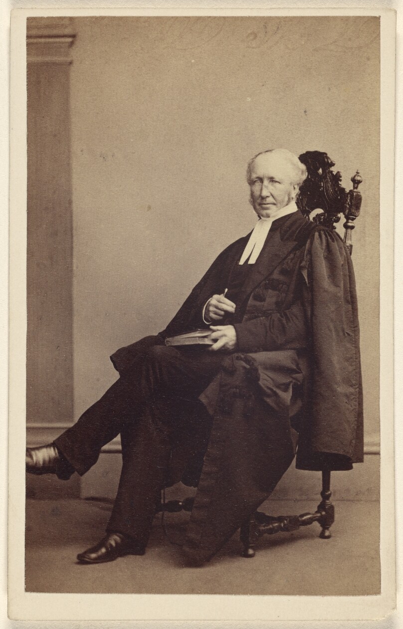 [Unidentified elderly man seated with a book in his lap, finger holding its place]