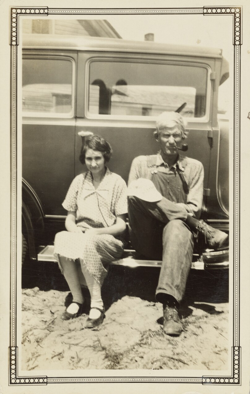 [Man and woman sitting on running board of car]